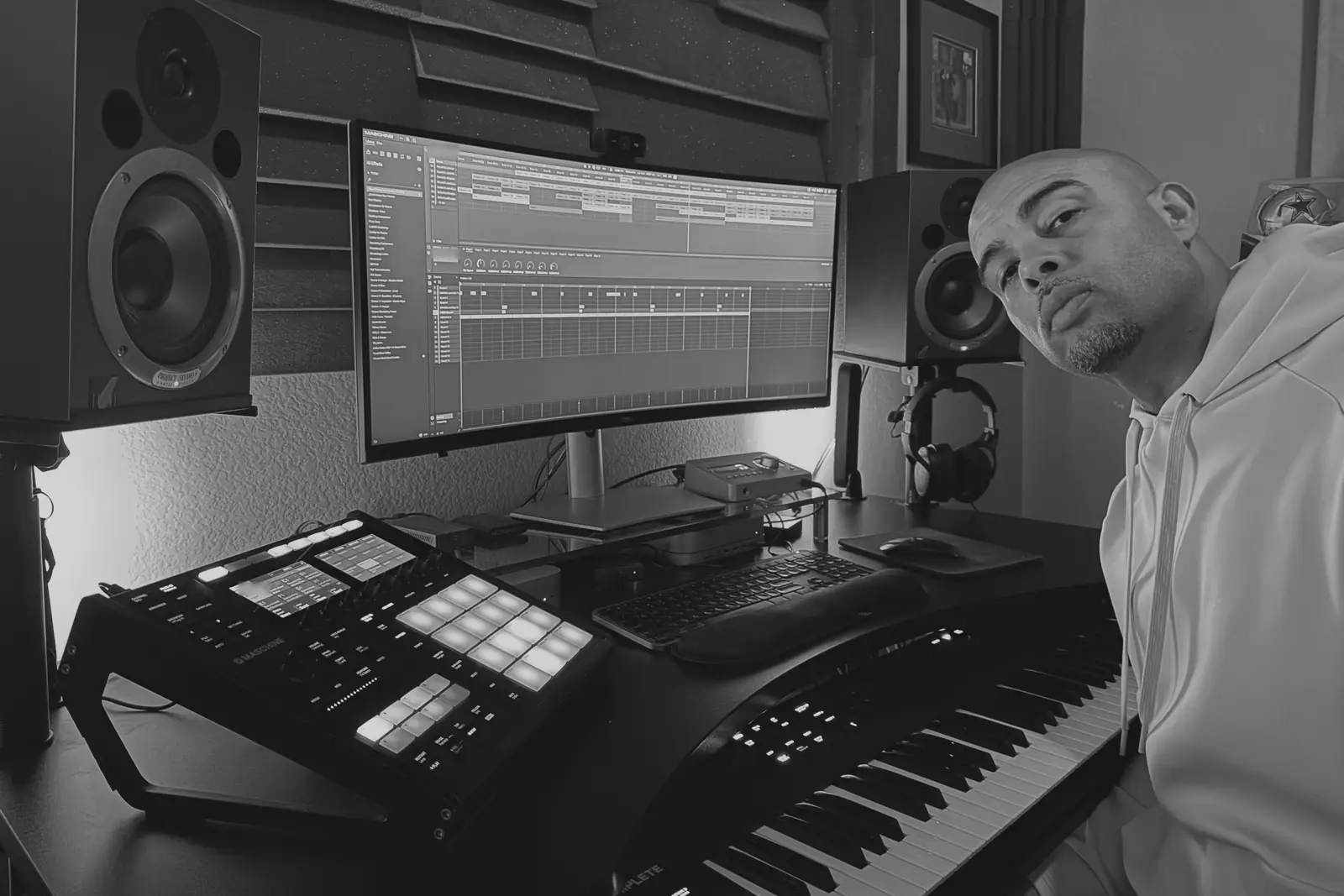 Moody in the studio, looking into the camera beside the Maschine, monitor and keys